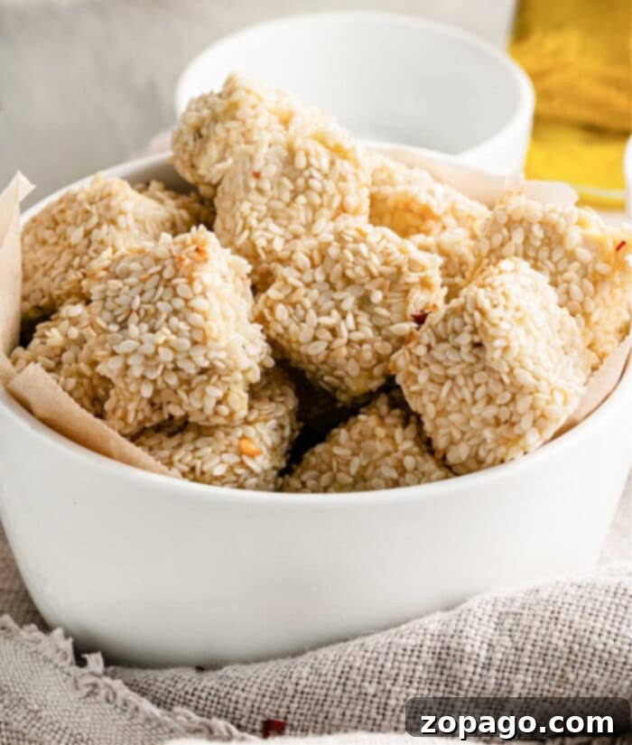 Crispy Tofu Bites 2 Crispy Baked Tofu Nuggets without breadcrumbs, coated in sesame seeds and golden brown, ready to be enjoyed.