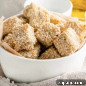 A white bowl filled with sesame-covered tofu nuggets rests on a cloth napkin.