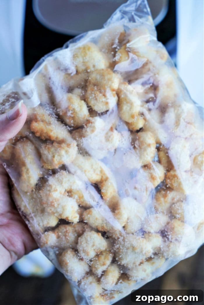 Perfectly Crispy Air Fryer Popcorn Shrimp 9 A hand holds a clear plastic bag filled with frozen breaded chicken nuggets, reminiscent of frozen popcorn shrimp ready for the air fryer. The nuggets are covered with frost, indicating they are icy and perfectly preserved. The background is slightly blurred and indistinct.