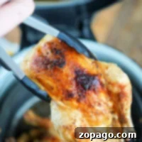 Tongs holding a piece of seasoned, cooked Cornish hen with crispy skin above a Ninja Foodi basket, perfect for achieving that ideal crispy texture.