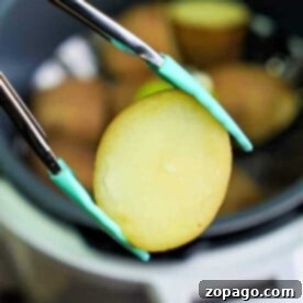 Close-up of tongs lifting a perfectly cooked potato slice from the bubbling Instant Pot.