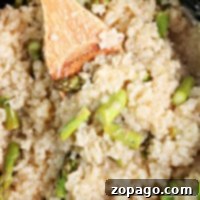 Close-up of creamy slow cooker risotto, with asparagus pieces being stirred gently with a wooden spoon.