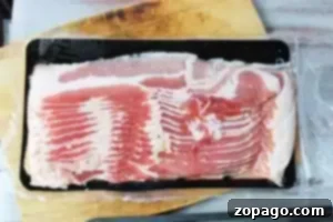A sealed package of uncooked bacon strips is placed on a wooden cutting board.