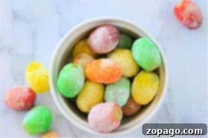 A bowl of colorful, sugar-coated gummy candies on a marble surface sits next to a guide on how to make candied grapes with Jello, adding an extra burst of creativity and flavor to your sweet treats.