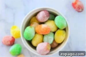 A bowl of colorful, sugar-coated gummy candies on a marble surface sits next to a guide on how to make candied grapes with Jello, adding an extra burst of creativity and flavor to your sweet treats.