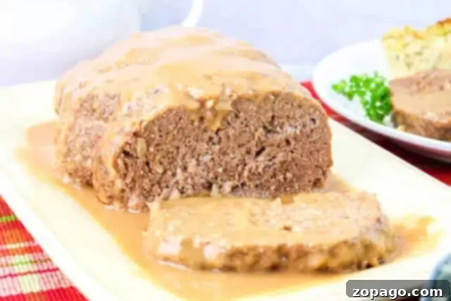 Ultimate Meatloaf Gravy 7 A plate of meatloaf topped with rich brown gravy for meatloaf recipe perfection sits on a light-colored platter. One slice is cut in the foreground. The dish rests on a red-and-yellow striped cloth, accompanied by a small bowl of green garnish in the background.
