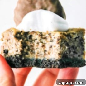 A hand holding a delectable slice of Oreo cheesecake, reminiscent of Philadelphia Cheesecake Bars, topped with whipped cream and a chocolate biscuit.