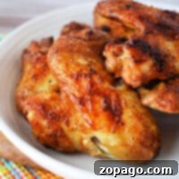 Crispy Air Fryer Whole Chicken Wings 6 Close-up of whole chicken wings, perfectly crisped in an air fryer, resting on a white plate atop a colorful checkered cloth.