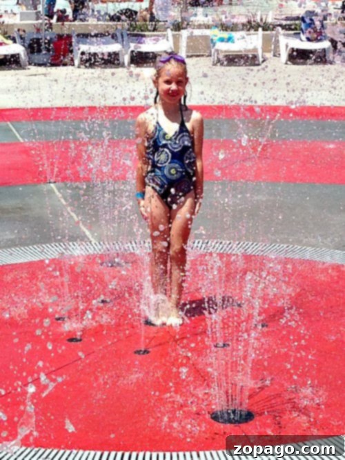 DropZone Water Park Perris What You Need To Know 3 Families enjoy the multi-level aquatic play structure at DropZone Waterpark in Perris, featuring colorful slides, sprayers, and a large tipping bucket, all designed for children's enjoyment.