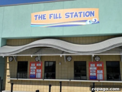 DropZone Water Park Perris What You Need To Know 9 The image shows an establishment called "The Fill Station" with a sign above and a wave-like awning, reminiscent of Perris Water Park. Below are three service windows with red menus posted on the wall. The building has a light green and yellow exterior.