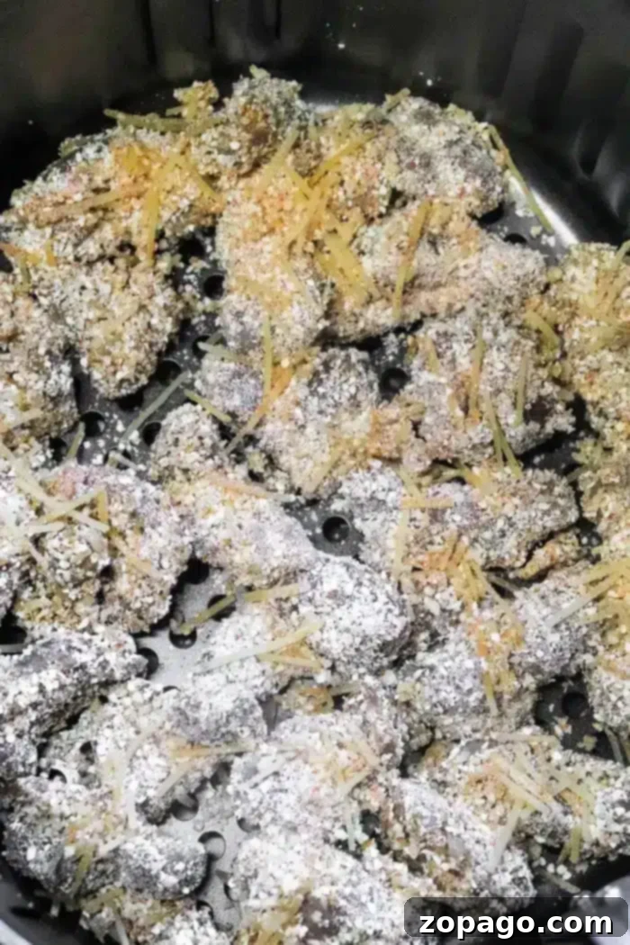 Golden Crispy Air Fryer Chicken Gizzards 7 Close-up of uncooked breaded meat pieces in an air fryer basket. The Air Fryer Chicken Gizzards are coated in a breadcrumb and grated cheese mixture, ready to be cooked. The air fryer basket shows standard perforations for air circulation.
