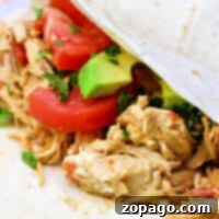 Quick Pressure Cooker Chicken Tacos 5 A close-up of a soft taco reveals pressure cooker chicken, infused with flavor, alongside sliced tomatoes, avocado, and cilantro on a white tortilla.