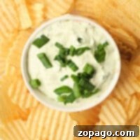A bowl of creamy Lawson's Chip Dip, topped with chopped green onions, is surrounded by crispy potato chips.