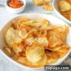 Russet Gold Crisps 6 A bowl of crispy russet potato chips sits elegantly with a small dish of ketchup in the background, inviting a delightful snacking experience.