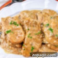 Succulent Slow Cooker Pork Chops with Velvety Gravy 6 Four tender Slow Cooker Pork Chops and Gravy, covered in rich brown sauce and garnished with chopped parsley, served on a white plate.