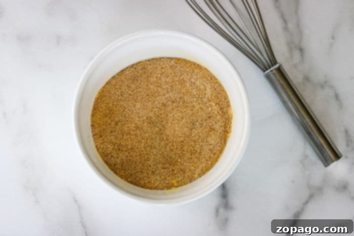 Recreate Lawrys Seasoned Salt At Home 4 A white bowl filled with freshly mixed homemade Lawry's seasoned salt, accompanied by a metal whisk on a elegant marble surface.