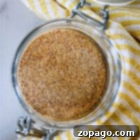 A glass jar filled with a seasoning blend, resting on a yellow-striped cloth, symbolizing homemade Lawry's Seasoned Salt.