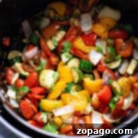 A vibrant mix of Mediterranean roast vegetables, including peppers, zucchini, onions, and herbs, nestled in a black pot, perfectly charred and aromatic from the air fryer.