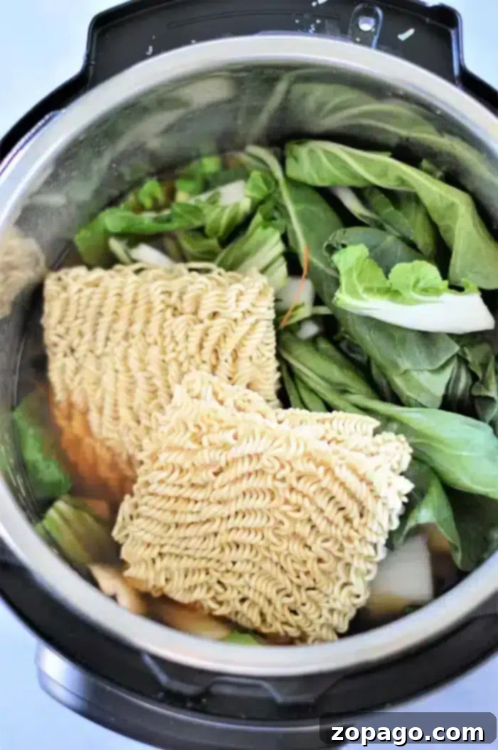 Perfect Instant Pot Ramen 9 The Instant Pot filled to the brim with colorful ingredients, depicting the stages of preparing a delightful vegetable ramen. Two blocks of dry instant noodles are carefully placed on top of a generous assortment of fresh, leafy greens and thinly sliced root vegetables, all gently submerged in a rich, savory broth, awaiting the pressure cooking process.
