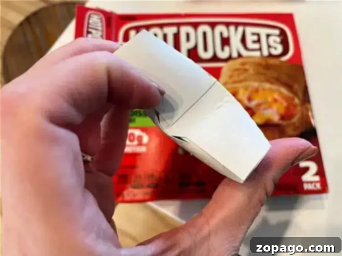No More Cold Spots Hot Pocket Cook Time Secrets 6 A hand holding an unfolded crisping sleeve with a Hot Pockets package in the background.