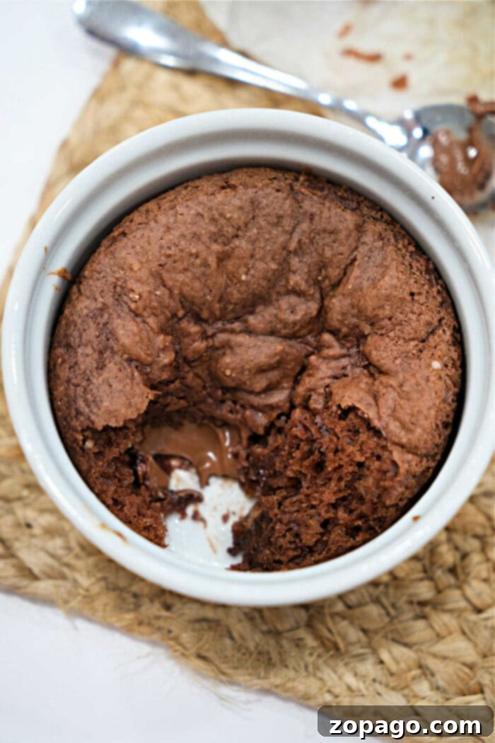 Mug Lava Cake Magic 6 Chocolate lava cake in a white ramekin with a spoonful missing, revealing gooey melted chocolate inside.
