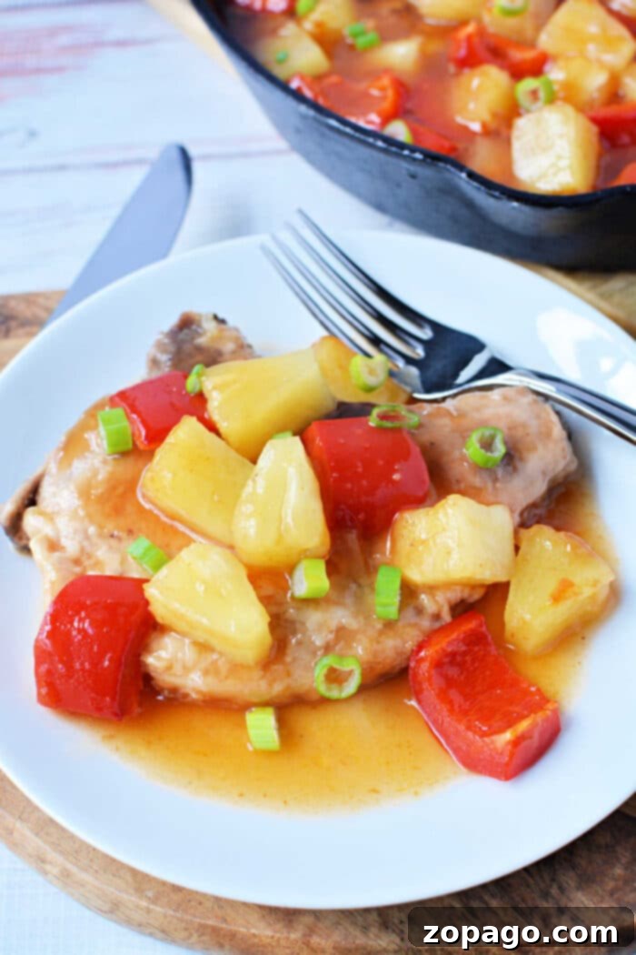 This dish features succulent pork chops topped with pineapple, red bell peppers, and sauce, then garnished with green onions on a white plate. A vibrant addition to your collection of pork chop recipes.