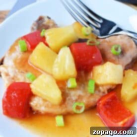 Tender pork chops and pineapple are topped with pineapple chunks, red bell peppers, sauce, and green onions, creating a vibrant dish served on a white plate.