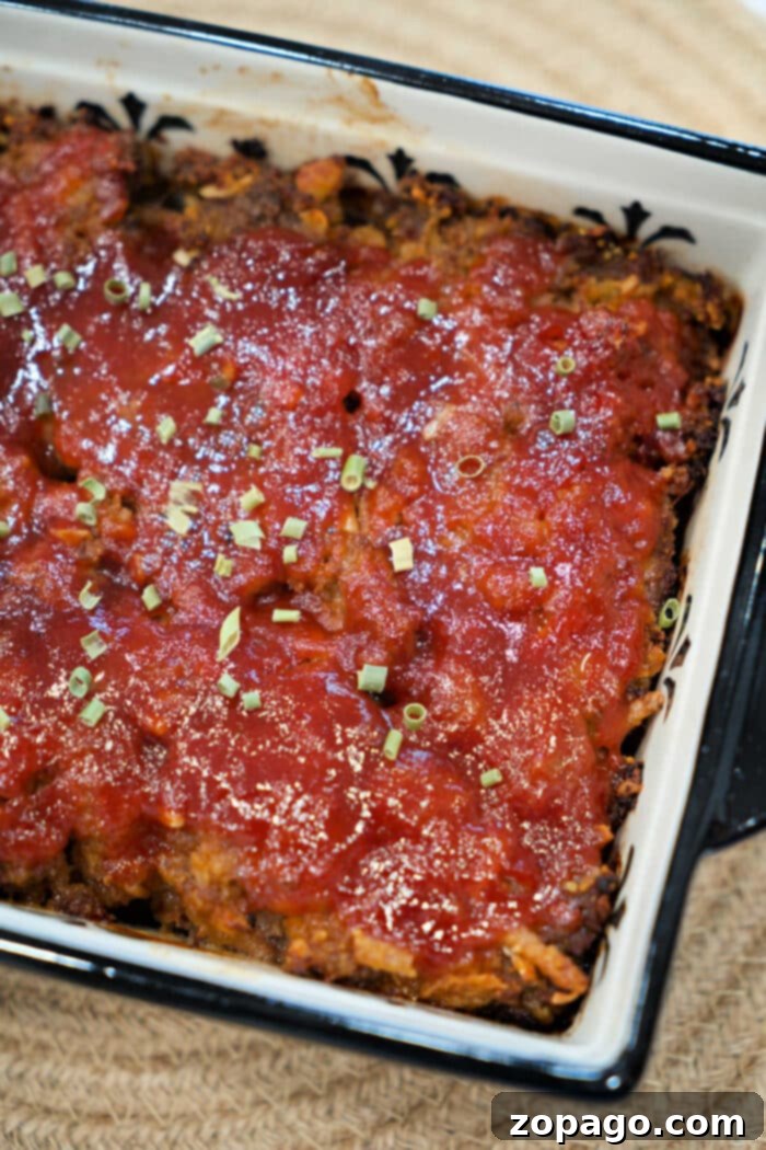 Smoky BBQ Meatloaf Perfection 2 A baked BBQ meatloaf topped with tomato sauce and chopped herbs in a rectangular dish.