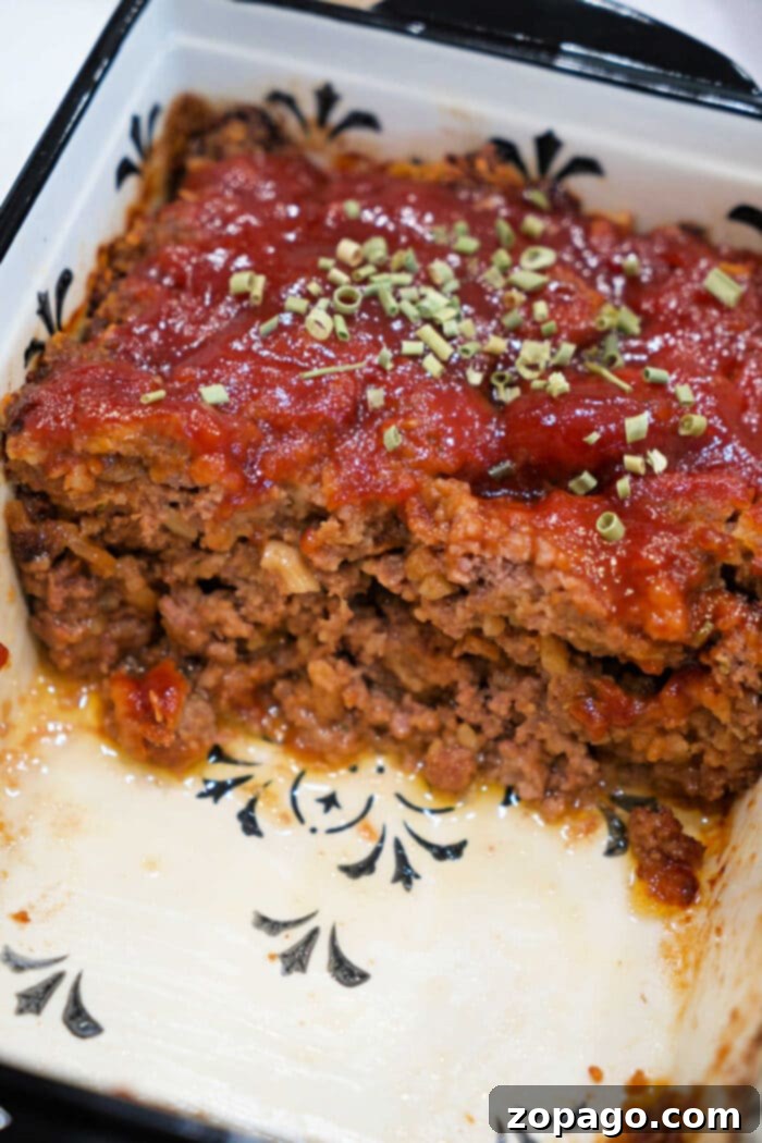 Smoky BBQ Meatloaf Perfection 6 A sliced meatloaf topped with tomato sauce and herbs in a white baking dish with a black pattern, perfect for trying a classic Meatloaf Recipe or transforming into a savory BBQ Meatloaf.