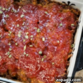 Smoky BBQ Meatloaf Perfection 7 A baked BBQ meatloaf topped with tomato sauce and chopped herbs in a rectangular dish.
