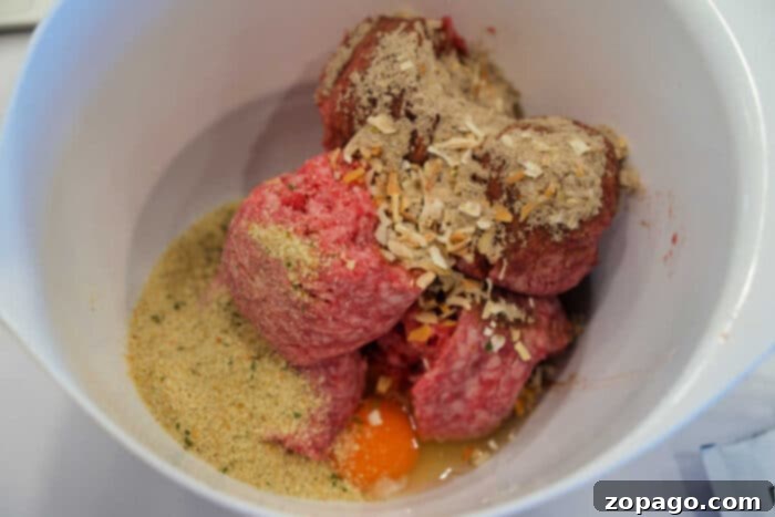Cheesy Baked Spaghetti Meatball Bake 3 Raw ground meat, breadcrumbs, spices, and a cracked egg in a white mixing bowl, ready to be mixed for delicious meatballs—perfect for pairing with baked spaghetti.