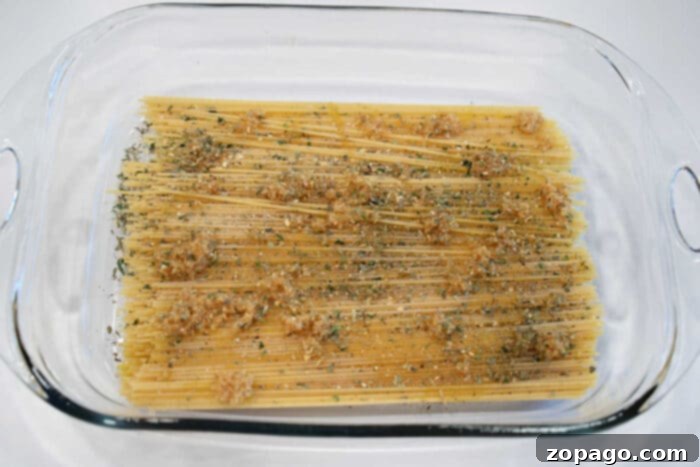 Cheesy Baked Spaghetti Meatball Bake 6 Uncooked spaghetti in a glass baking dish, topped with minced garlic and dried herbs, ready to be transformed into a classic baked spaghetti with meatballs.