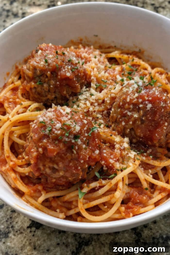 Cheesy Baked Spaghetti Meatball Bake 8 Baked spaghetti with meatballs topped with tomato sauce, grated cheese, and herbs, served in a white bowl on a granite counter.