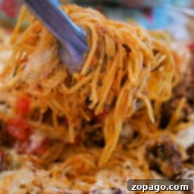 Tongs lifting cheesy baked spaghetti with meatballs from a casserole dish, showcasing gooey cheese and savory meatballs in every bite.