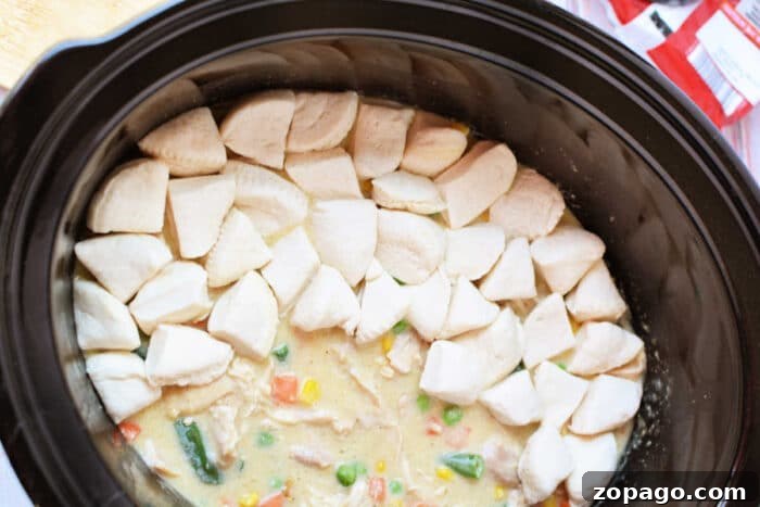 Slow-Cooker Chicken Pot Pie: Creamy One-Pot Dinner Recipe 6 Crockpot Chicken and vegetable stew in a slow cooker, topped with raw biscuit dough pieces arranged in a ring for a delicious twist on classic Chicken Pot Pie.