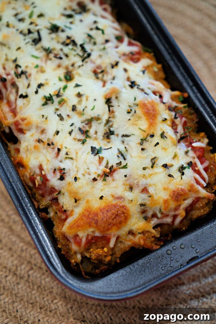 Chicken Parmesan Meatloaf Recipe That Melts in Your Mouth 2 Baked Chicken Parmesan Meatloaf casserole topped with melted cheese and herbs in a rectangular dish on a woven placemat.