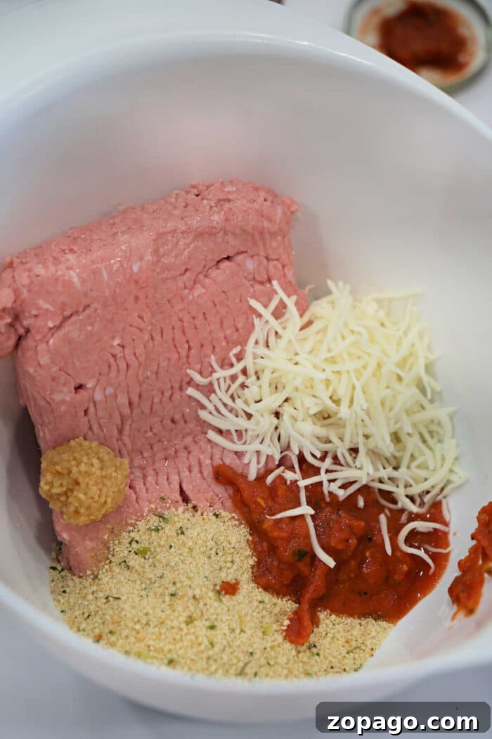 Chicken Parmesan Meatloaf Recipe That Melts in Your Mouth 3 Ground meat, shredded cheese, breadcrumbs, minced garlic, and tomato sauce in a white mixing bowl—perfect for preparing a flavorful Chicken Parmesan Meatloaf.