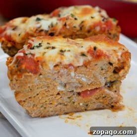 Chicken Parmesan Meatloaf Recipe That Melts in Your Mouth 6 Two slices of cheesy, baked Chicken Parmesan Meatloaf topped with tomato sauce and herbs sit on a white plate.