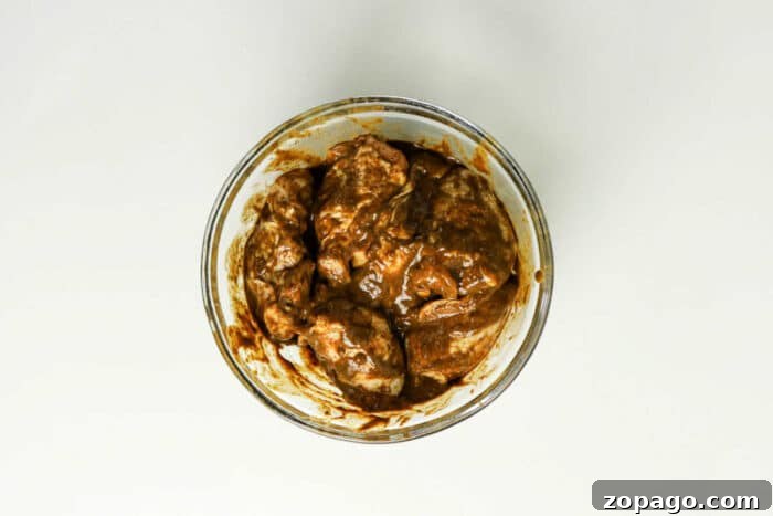Oven-Baked Jerk Chicken Recipe with Crispy Skin and Spicy Glaze 4 Glass bowl with pieces of meat coated in a thick brown jerk chicken marinade, ready for the oven, placed on a white surface—a perfect start to your favorite jerk chicken recipe.