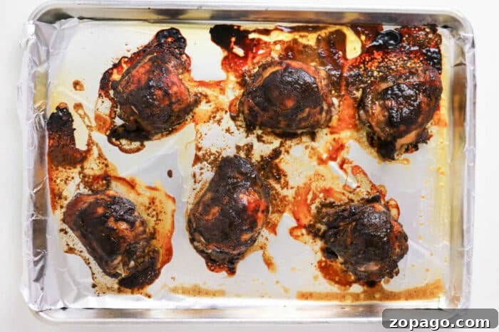Oven-Baked Jerk Chicken Recipe with Crispy Skin and Spicy Glaze 5 Six oven jerk chicken thighs on a foil-lined baking sheet, with browned and crispy skin and flavorful juices around them.