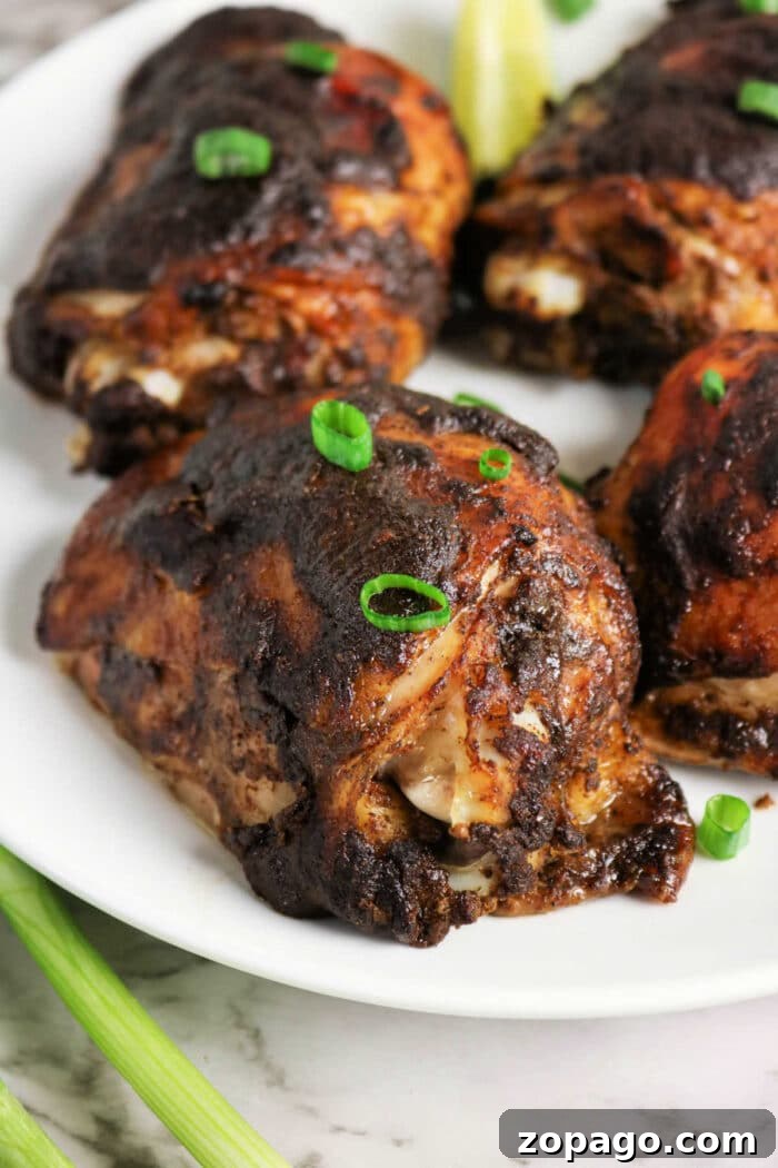 Oven-Baked Jerk Chicken Recipe with Crispy Skin and Spicy Glaze 6 Four pieces of dark, grilled Jerk Chicken garnished with green onions, served on a white plate.