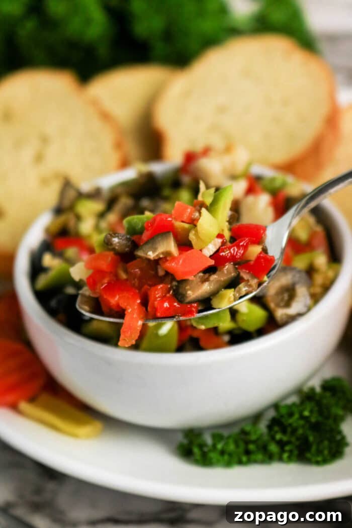 Authentic Muffuletta Olive Salad Recipe for Sandwichs & Platters 5 A spoonful of mixed chopped vegetables above a bowl, hinting at a classic Olive Salad recipe, with bread slices in the background.