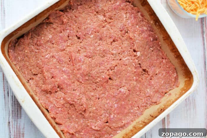 Mac and Cheese Meatloaf Casserole Bake 4 Raw ground meat mixture spread evenly in a square baking dish, ready to be cooked into a hearty meatloaf casserole.