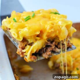 Mac and Cheese Meatloaf Casserole Bake 7 A spatula lifts a cheesy meatloaf casserole from a baking dish, topped with melted cheese and chives, blending classic casserole comfort with the creamy goodness of mac and cheese.