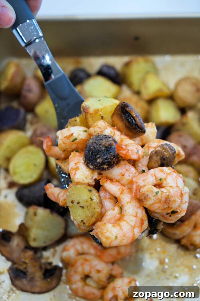 Garlic Butter Shrimp with Crispy Roasted Potatoes 2 A spoon holds shrimp and potatoes with mushrooms above a tray filled with roasted shrimp and potatoes, plus savory mushrooms.