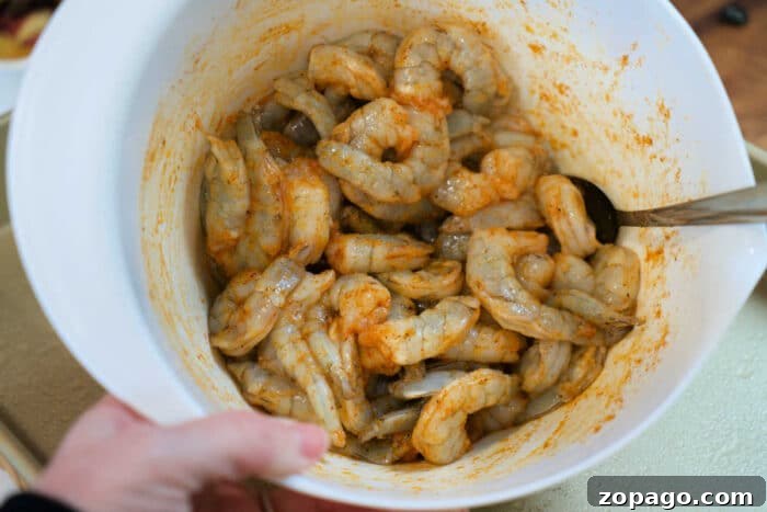 Garlic Butter Shrimp with Crispy Roasted Potatoes 3 A bowl of raw shrimp and potatoes marinated with spices, being mixed with a spoon.