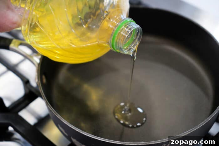 Crispy Fried Tilapia with Lemon and Herbs 4 Vegetable oil being poured from a plastic bottle into a black frying pan on a stovetop, ready for preparing a delicious fried tilapia recipe.