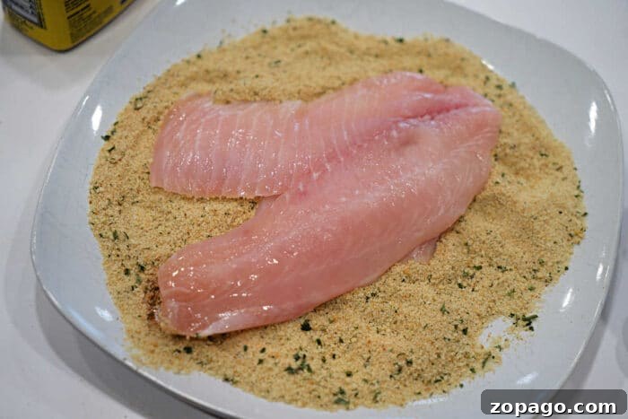 Crispy Fried Tilapia with Lemon and Herbs 5 Raw fish fillets on a plate of seasoned bread crumbs, ready for coating and cooking—a classic start to any delicious Fried Tilapia recipe.