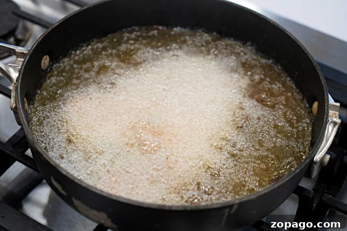 Crispy Fried Tilapia with Lemon and Herbs 6 A black pan on a stove with fried tilapia deep frying in bubbling hot oil, perfect for your next tilapia recipe.