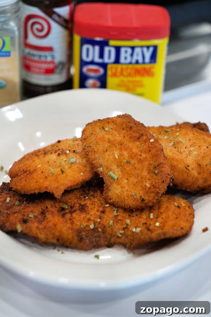 Crispy Fried Tilapia with Lemon and Herbs 7 A plate of golden, breaded fried chicken cutlets, garnished with herbs, with seasoning containers behind—perfect for those who love a great Fried Tilapia or classic chicken dish.